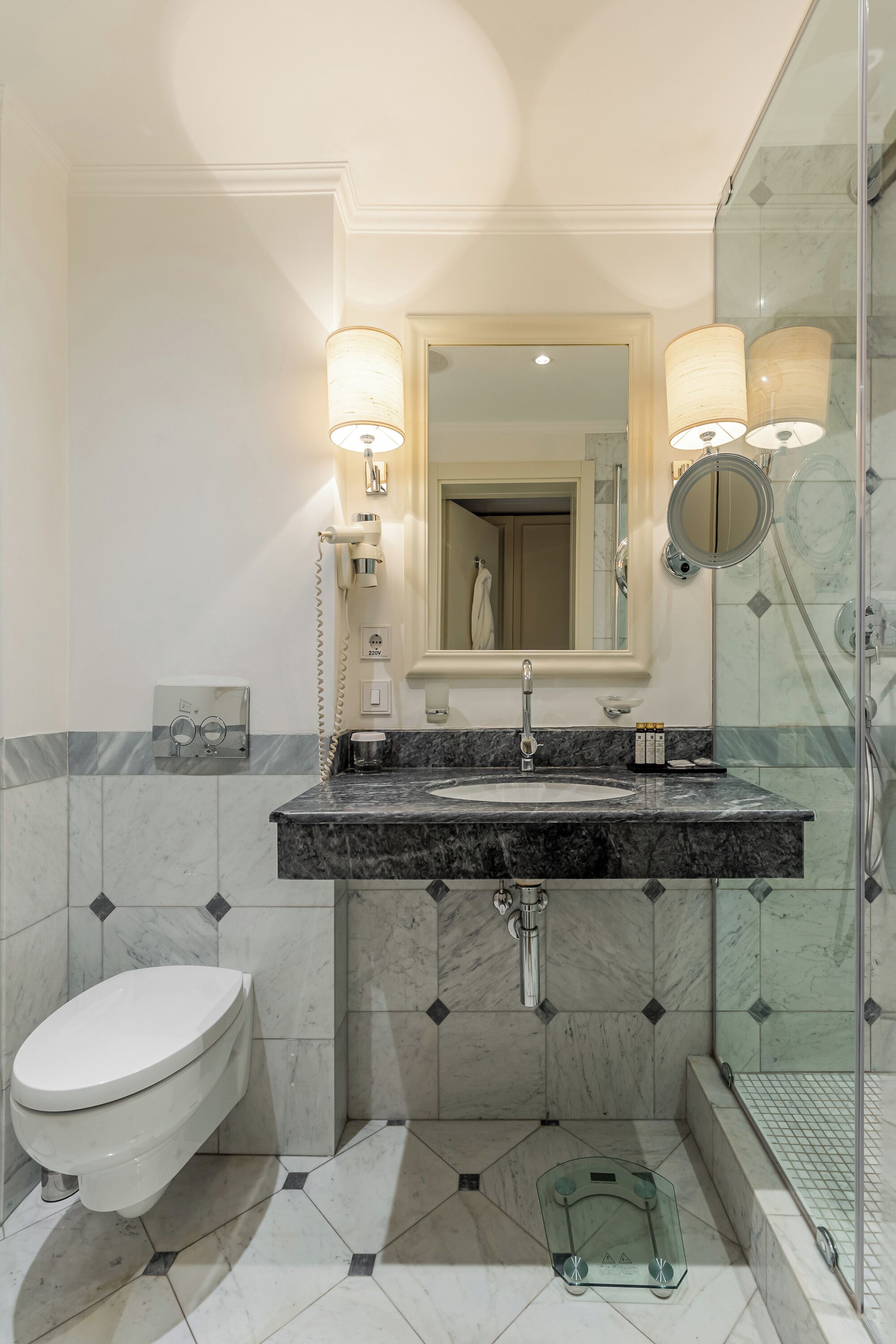 A bathroom with a marble sink, a toilet, and a glass shower enclosure.