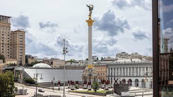 A tall monument with a statue on top, surrounded by a plaza with a modern building in the background.
