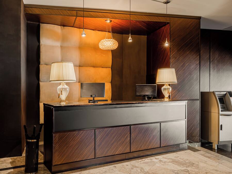 A reception desk with a modern design, featuring a dark wood finish, two lamps, and a digital screen.