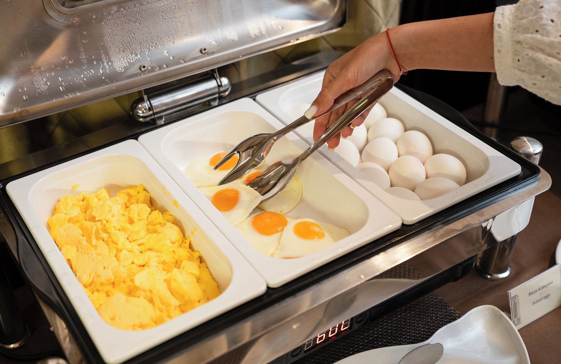 A buffet setup with scrambled eggs, fried eggs, and a container of mashed potatoes.