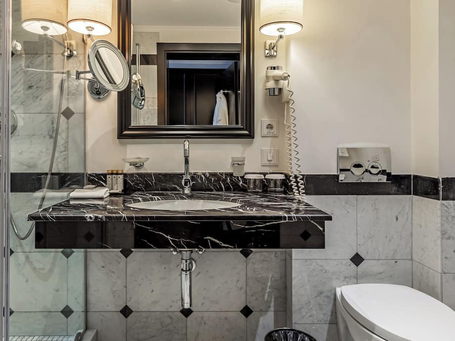Une salle de bain avec un lavabo en marbre, un miroir, des toilettes et une poubelle.