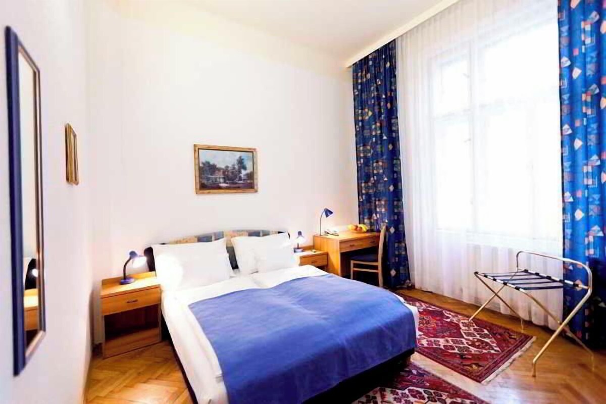 Hotellihuone, jossa on sänky, työpöytä, tuoli, ikkuna verhoilla ja seinälle ripustettu taulu.