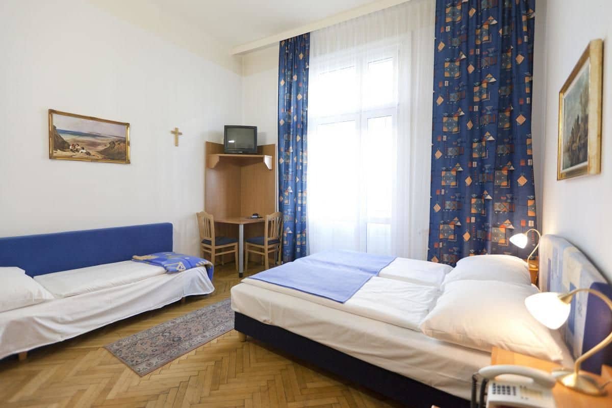 A room with two beds, a desk, a chair, a television, and a cross on the wall.