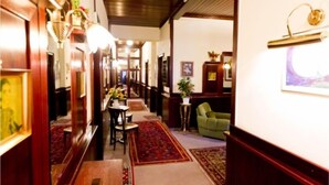 A hotel corridor with wooden paneling, a reception desk, a green armchair, and a red carpet. - Hotel-Pension Bleckmann (Vienna)