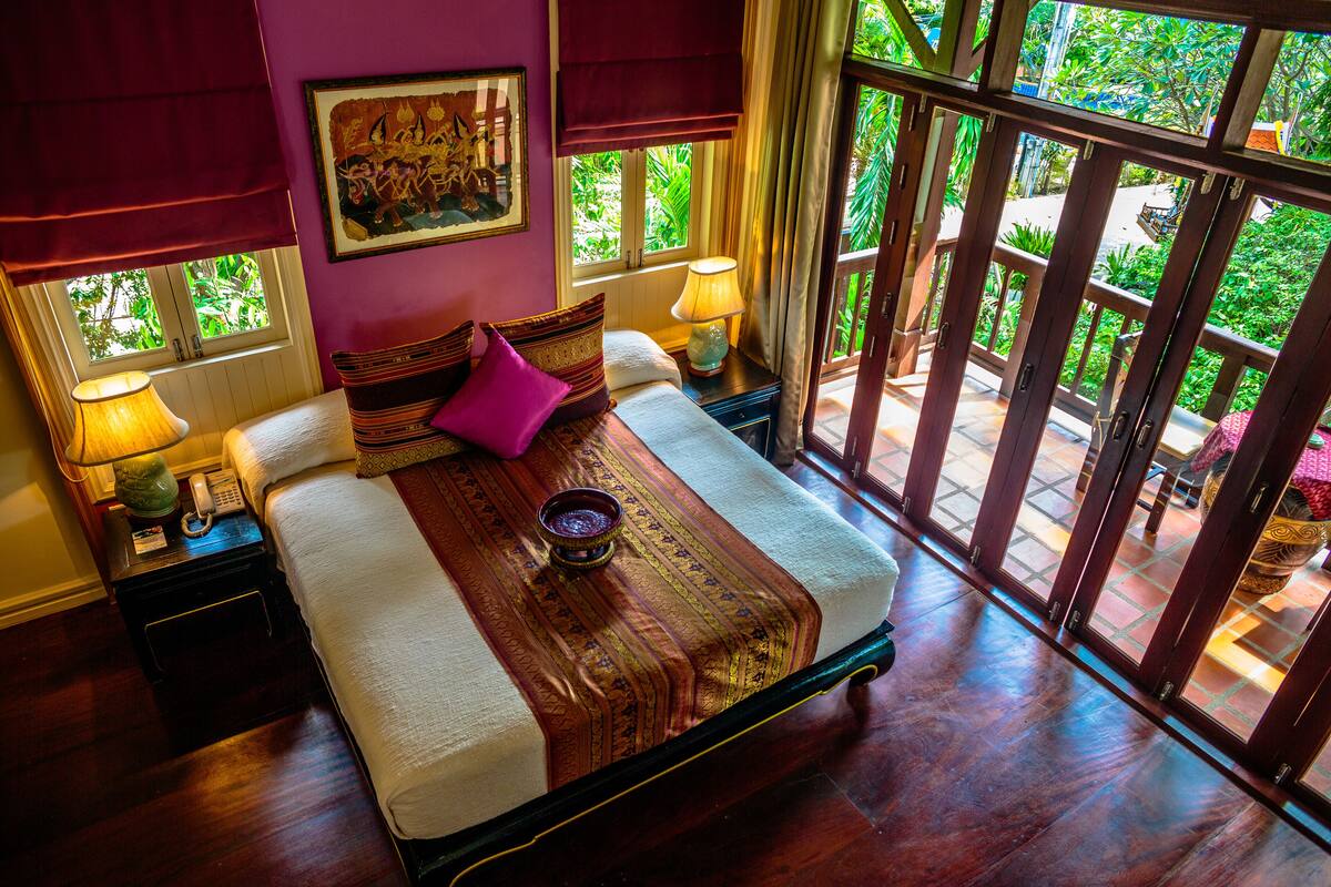 A bed with a wooden headboard, two bedside lamps, and a window with a view of greenery.