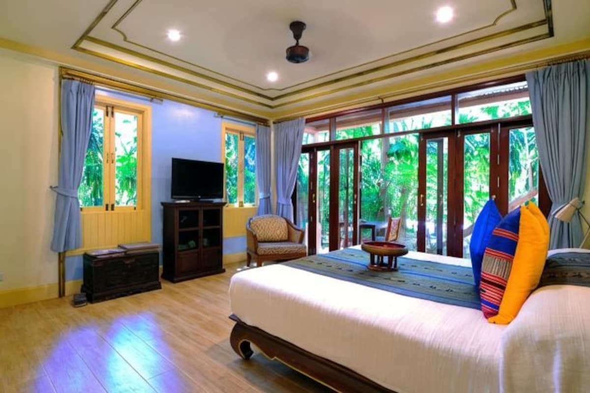 A bedroom with a large bed, a television on a stand, a chair, and a view through the window.