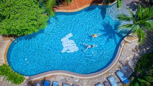 Vue aérienne d’une piscine dotée d’une mosaïque au motif original, entourée de chaises longues et de palmiers.