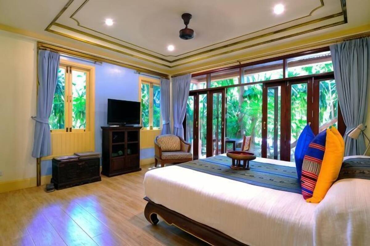 A bedroom with a large bed, a television on a stand, a chair, and a view through the window.