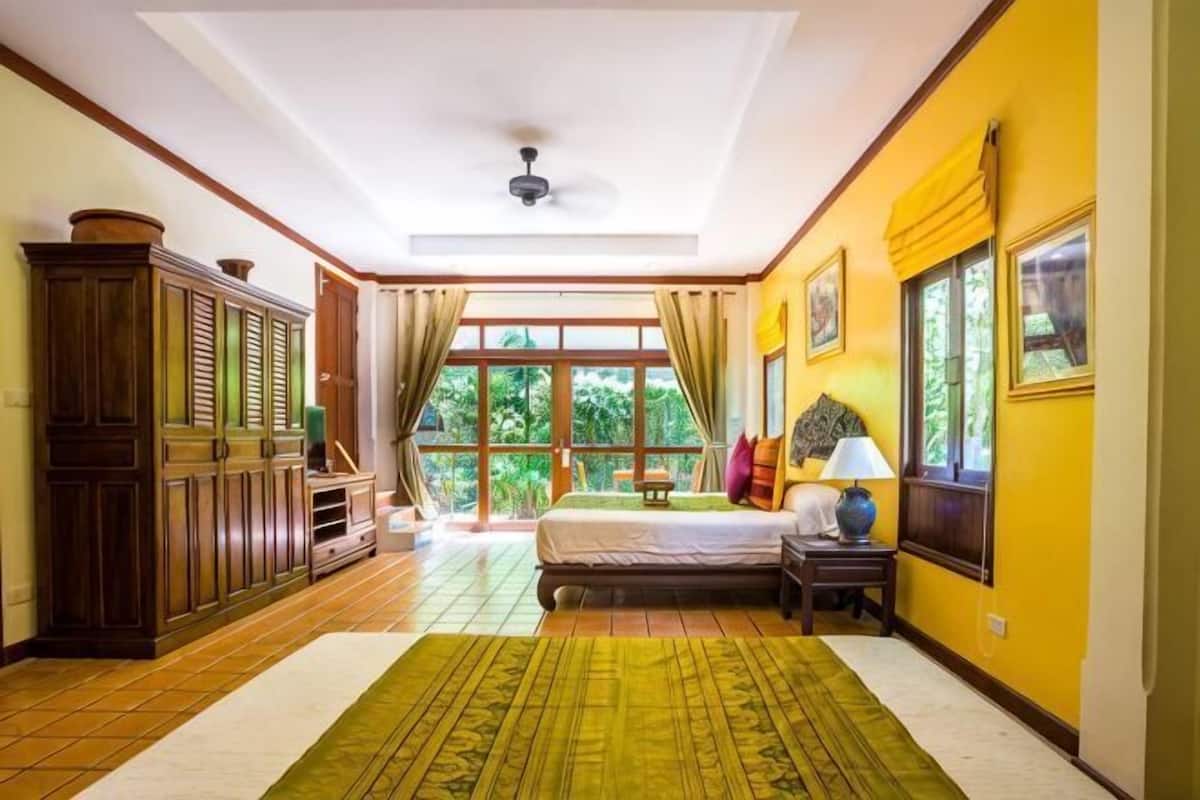 A room with a bed, a nightstand, a window with curtains, a wooden cabinet, and a ceiling fan.