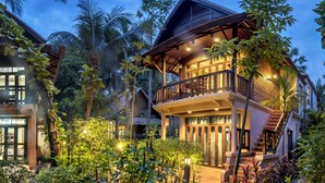 Une maison à deux étages dotée d’un balcon, entourée d’une végétation luxuriante et d’un jardin bien entretenu.