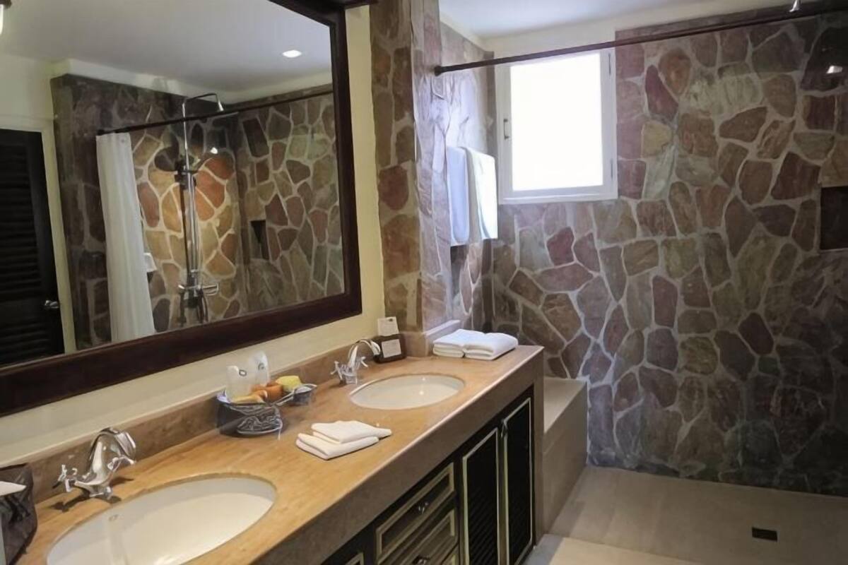 A bathroom with two sinks, a large mirror, and a shower area with stone walls.