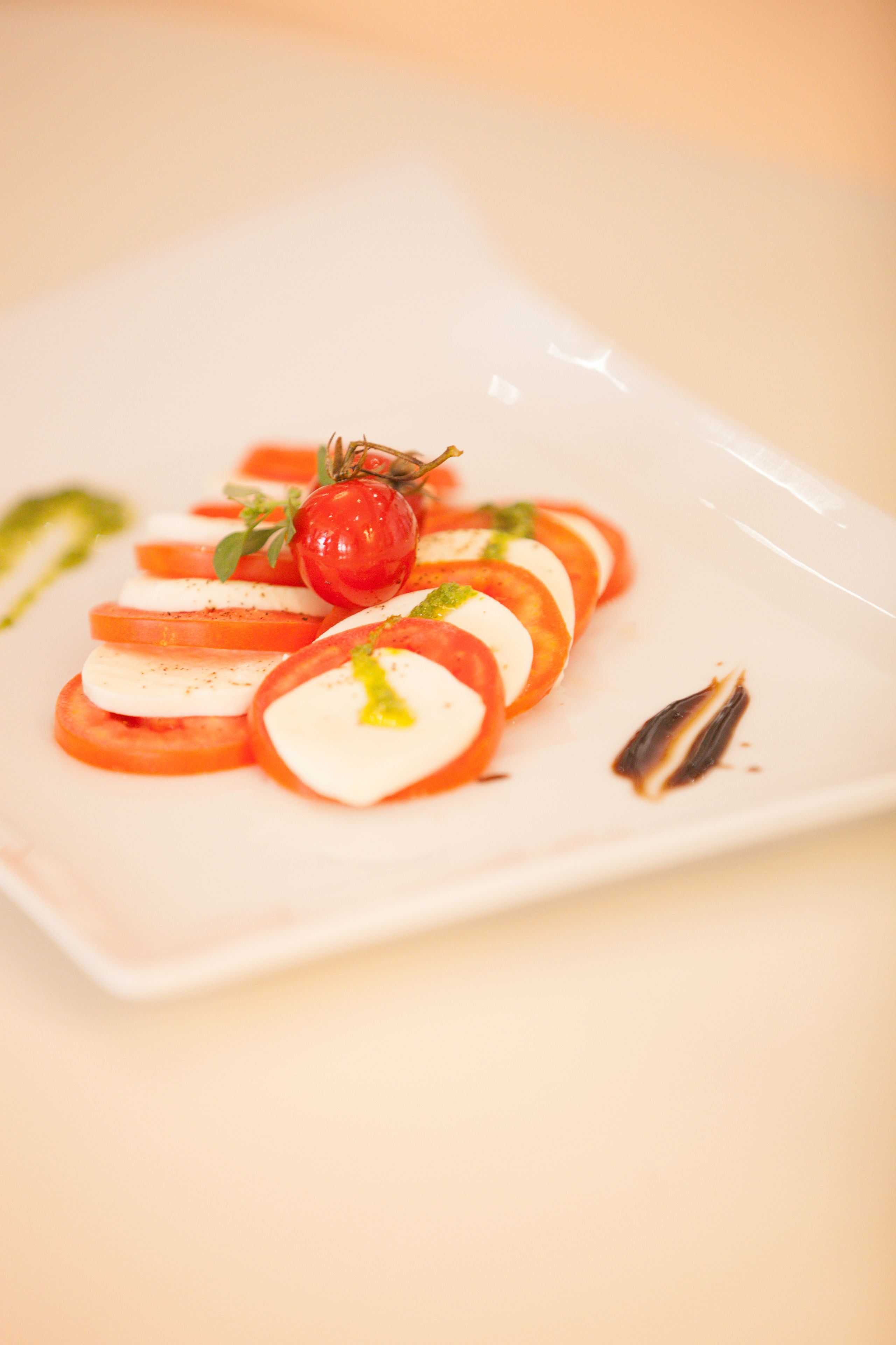A white rectangular plate with a tomato and mozzarella salad, garnished with a cherry tomato and basil leaves.