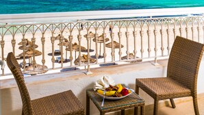 A balcony with wicker chairs and a table with fruit, overlooking a beach with thatched umbrellas and a clear blue sea. - Sousse Palace Hotel & Spa (Sousse)
