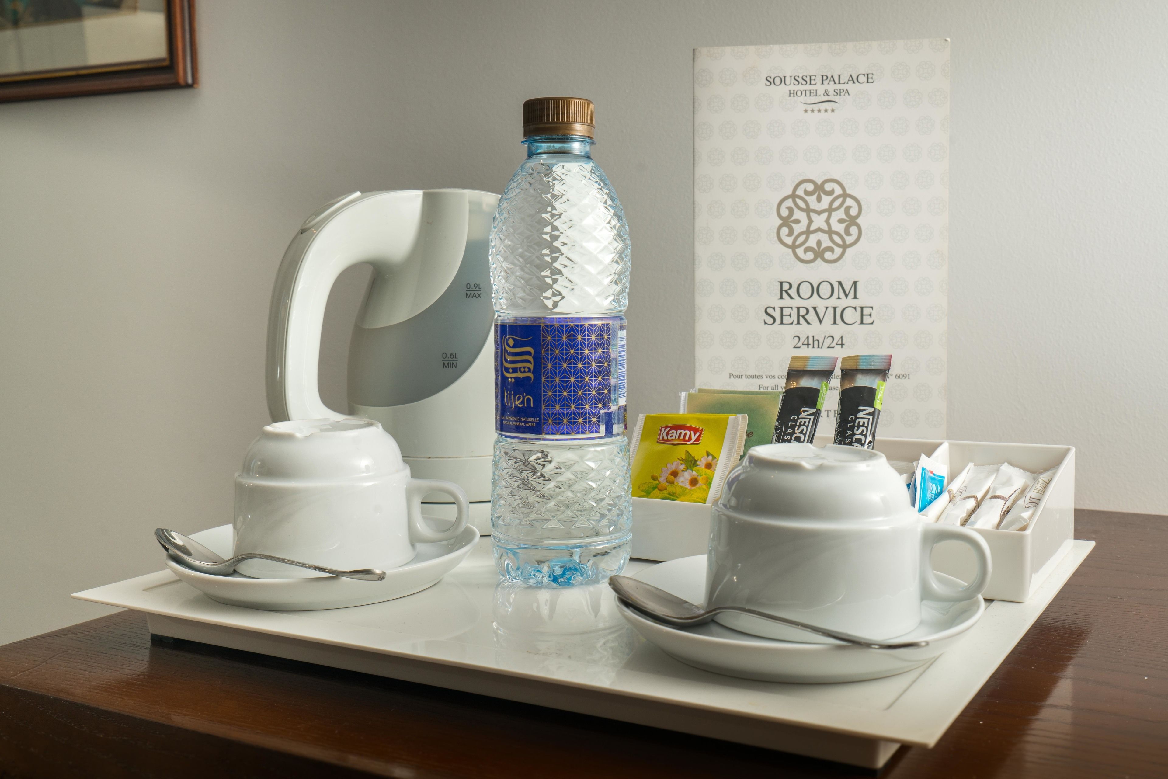 Een roomservice karretje met een waterfles, bekertjes en een dienblad met theezakjes.