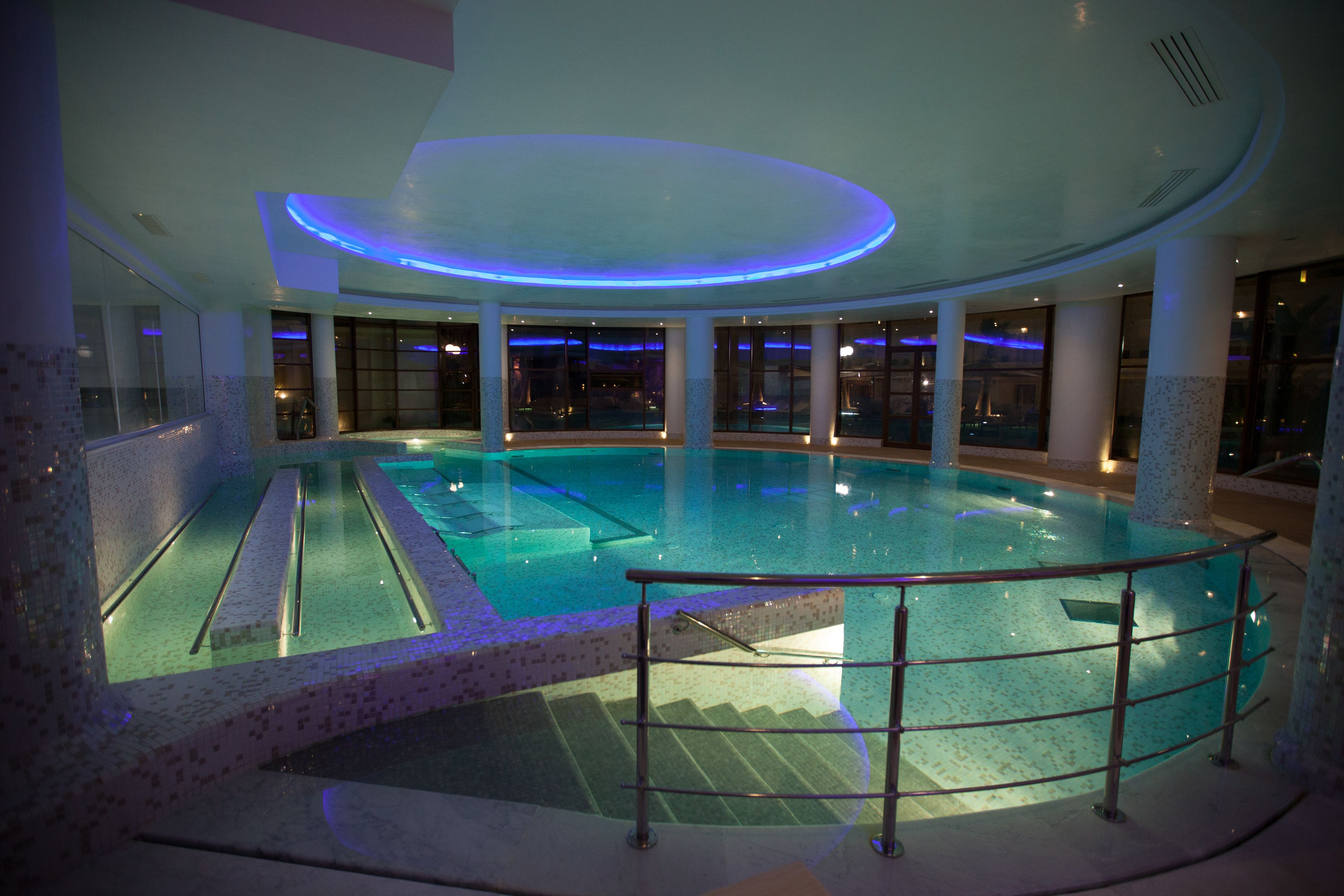 Una piscina interior con barrera de vidrio, suelo de baldosas y un diseño moderno en el techo.