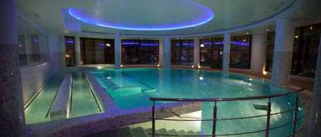 Una piscina interior con barrera de vidrio, suelo de baldosas y un diseño moderno en el techo.