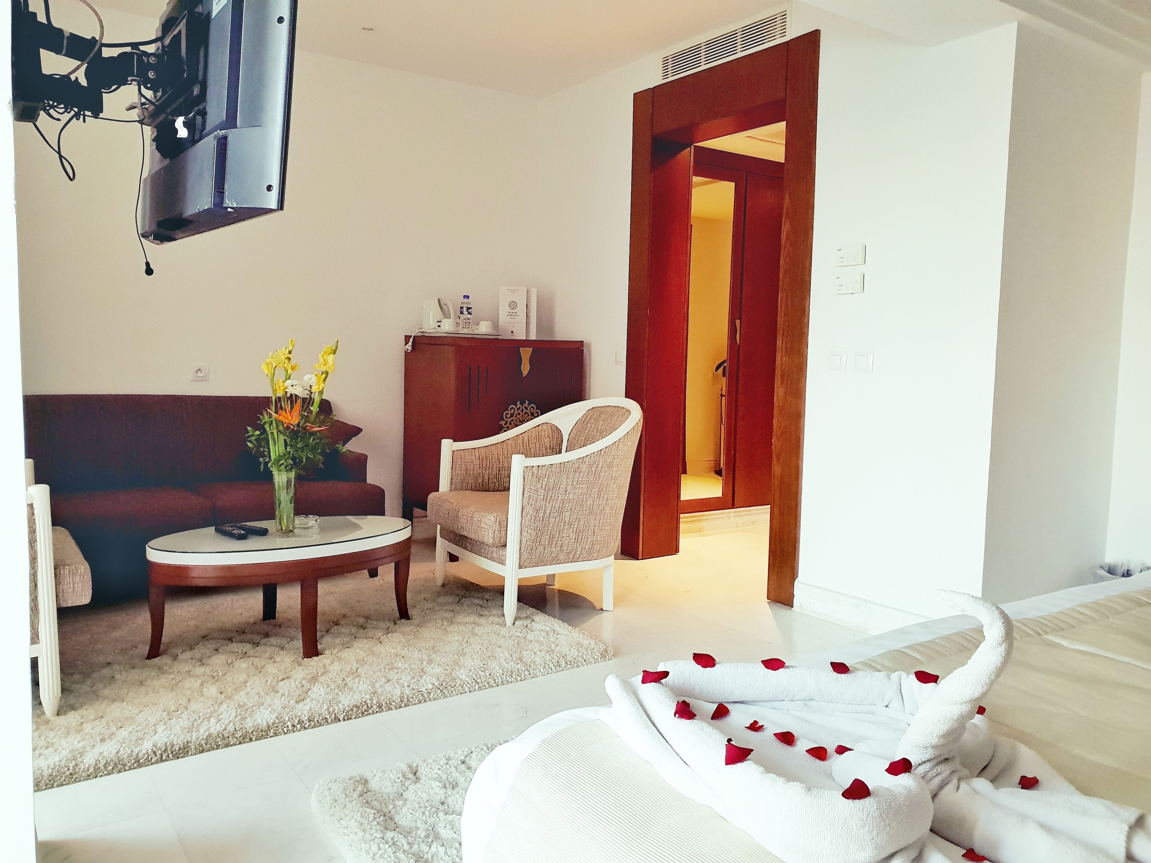 Ein Wohnzimmer mit einer Couch, einem runden Couchtisch, einem weißen Sessel und einem Zierhandtuch mit Rosenblüten.