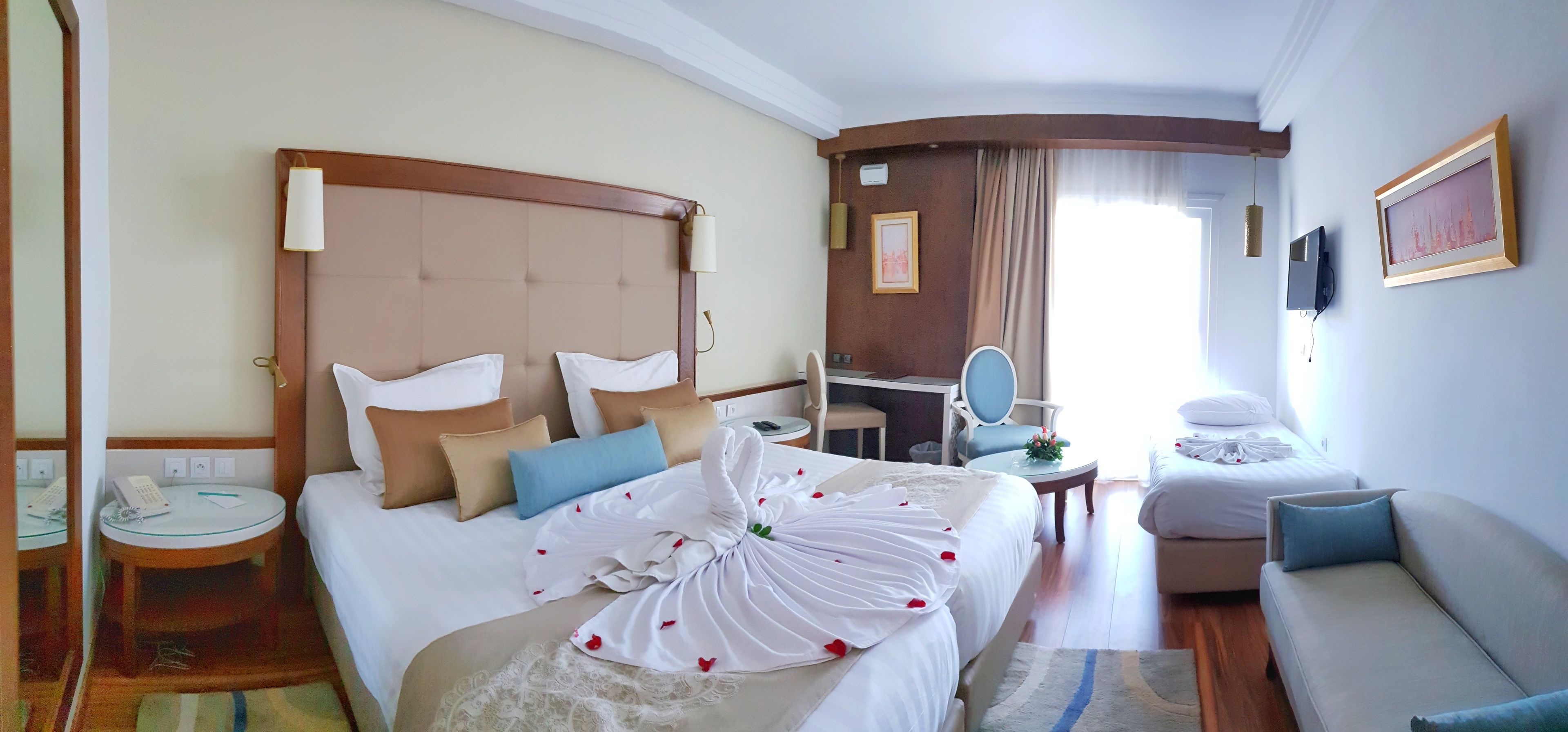A hotel room with a large bed, a desk, a chair, a sofa, and a television.