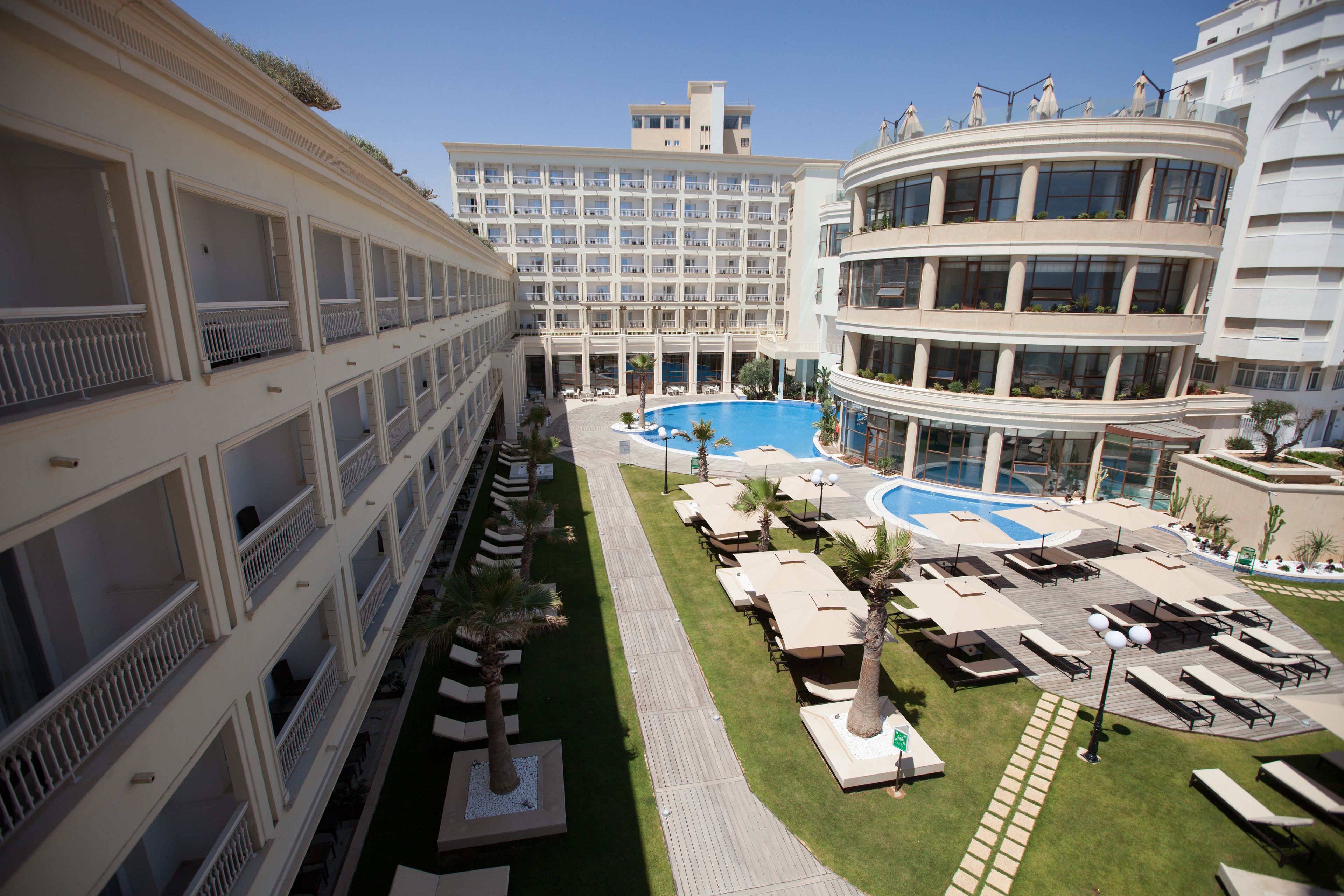 Un hôtel à étages, doté d’un espace piscine central avec des chaises longues et d’une pelouse bien entretenue.