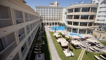 Un hôtel à étages, doté d’un espace piscine central avec des chaises longues et d’une pelouse bien entretenue.
