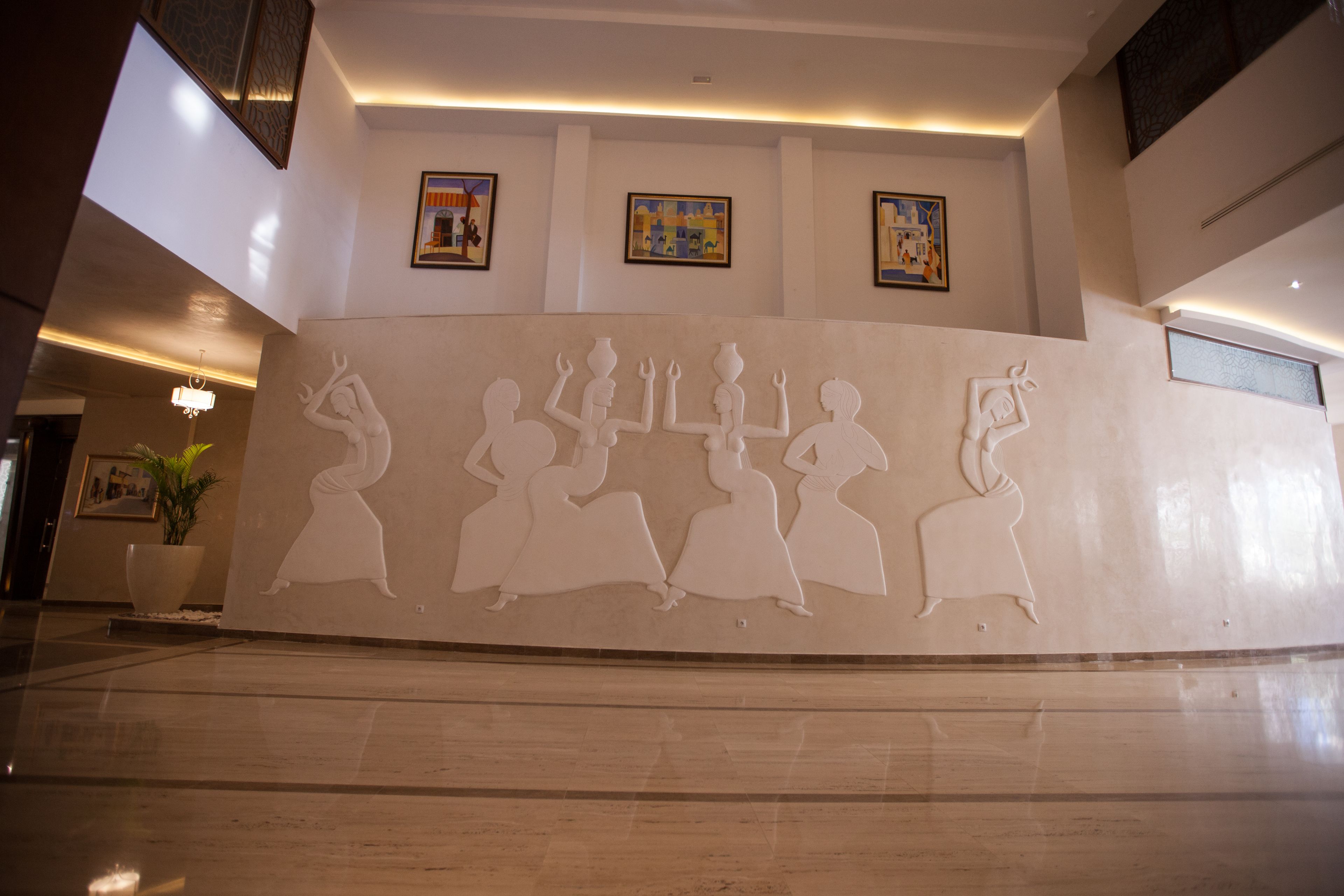 A lobby with a large wall mural of dancing figures, a potted plant, and framed artwork on the walls.