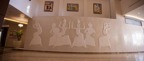 A lobby with a large wall mural of dancing figures, a potted plant, and framed artwork on the walls.