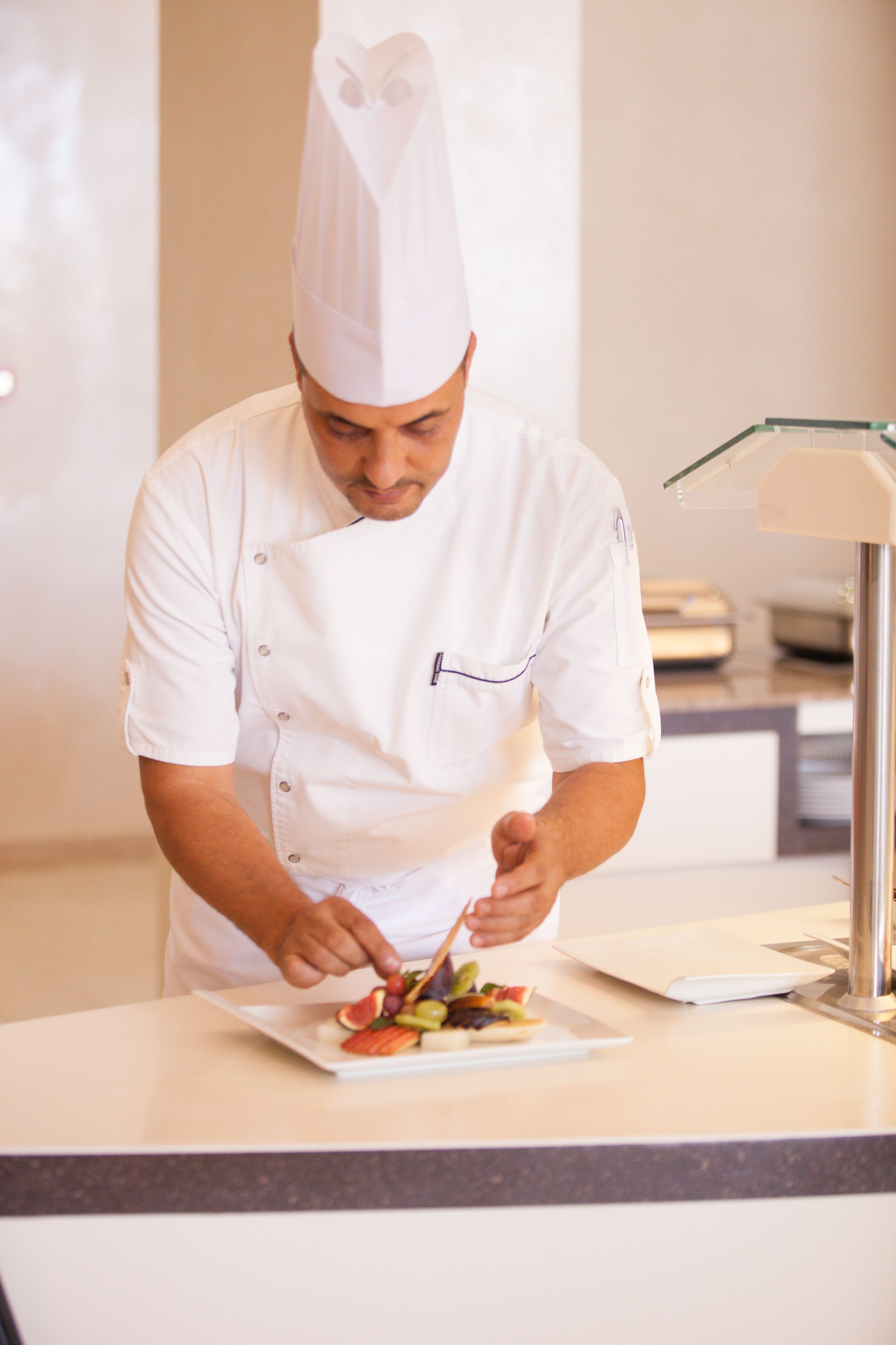 Un chef con uniforme blanco prepara un plato sobre una encimera en una cocina de diseño moderno.