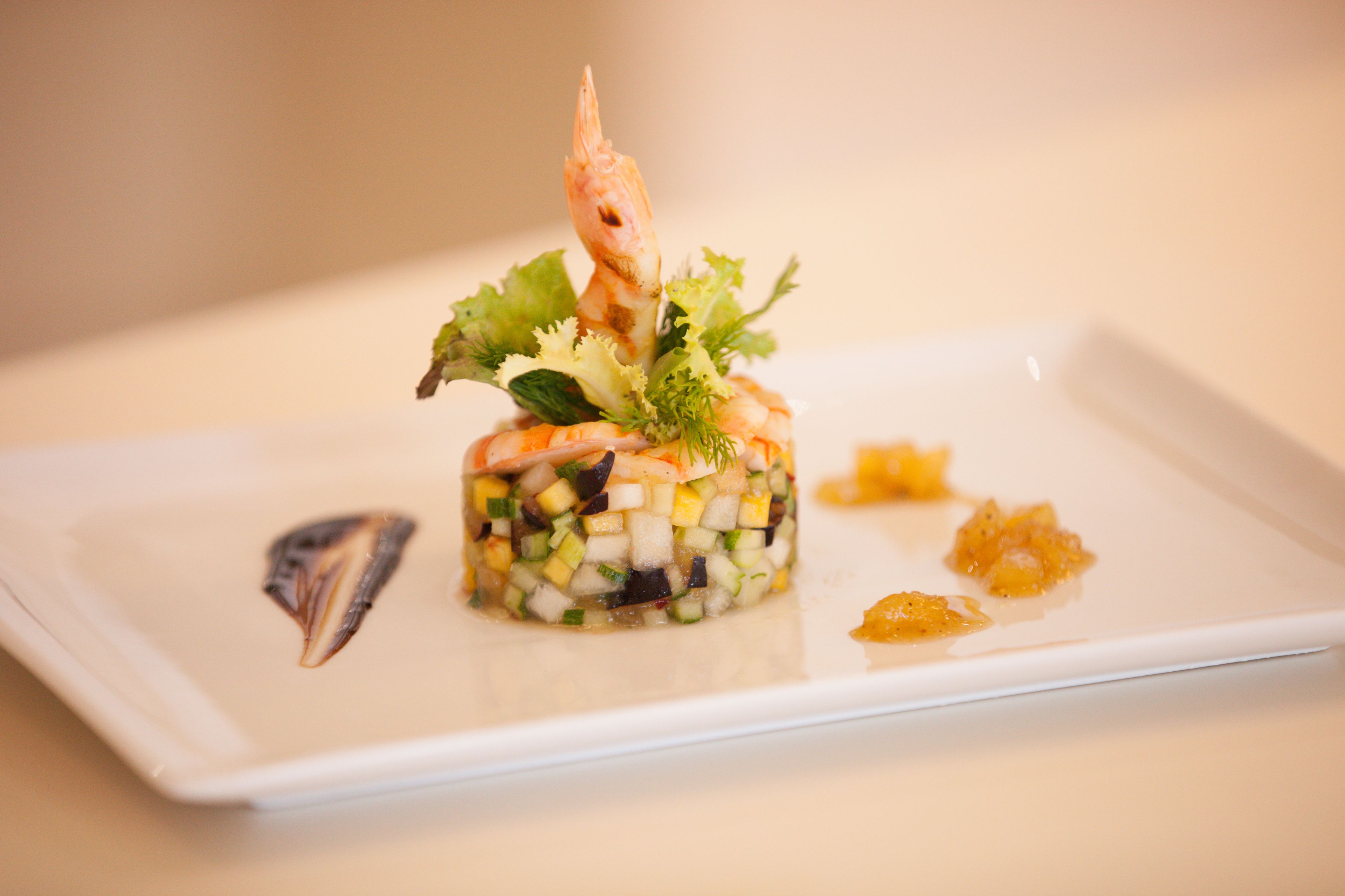 A dish with a shrimp on top, surrounded by vegetables and garnishes, served on a white plate.