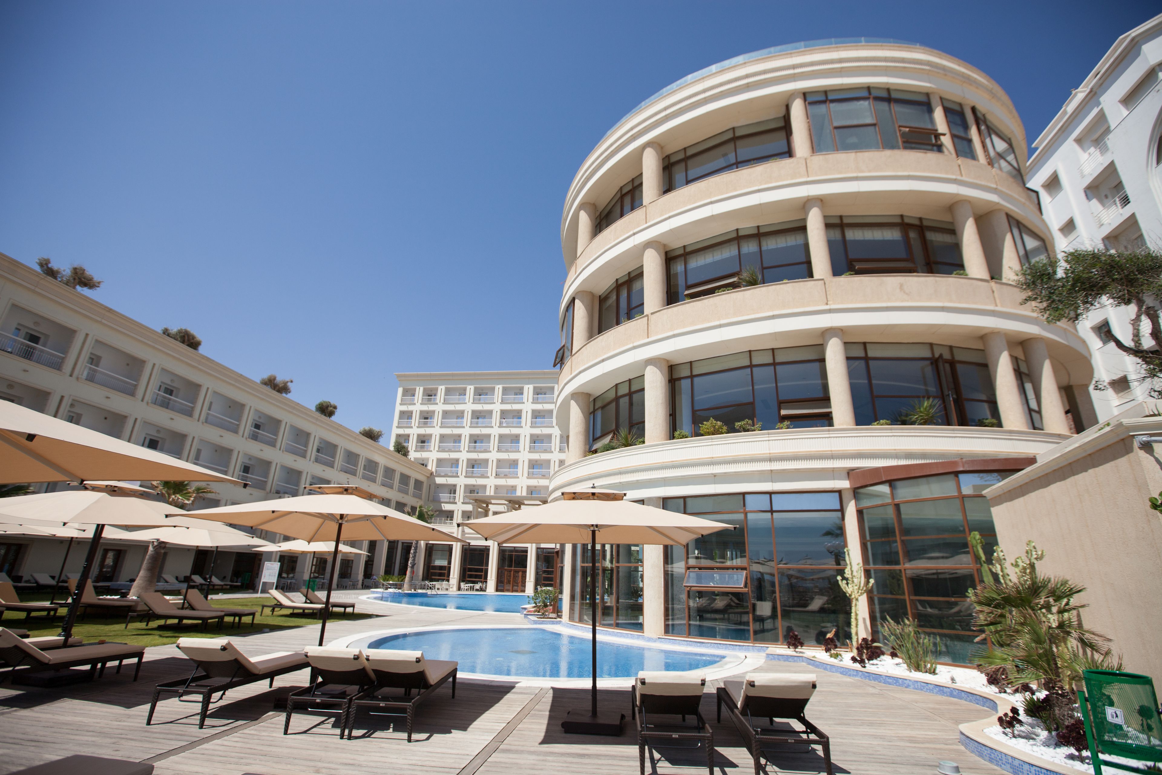 A hotel with a pool area, sun loungers, and umbrellas.