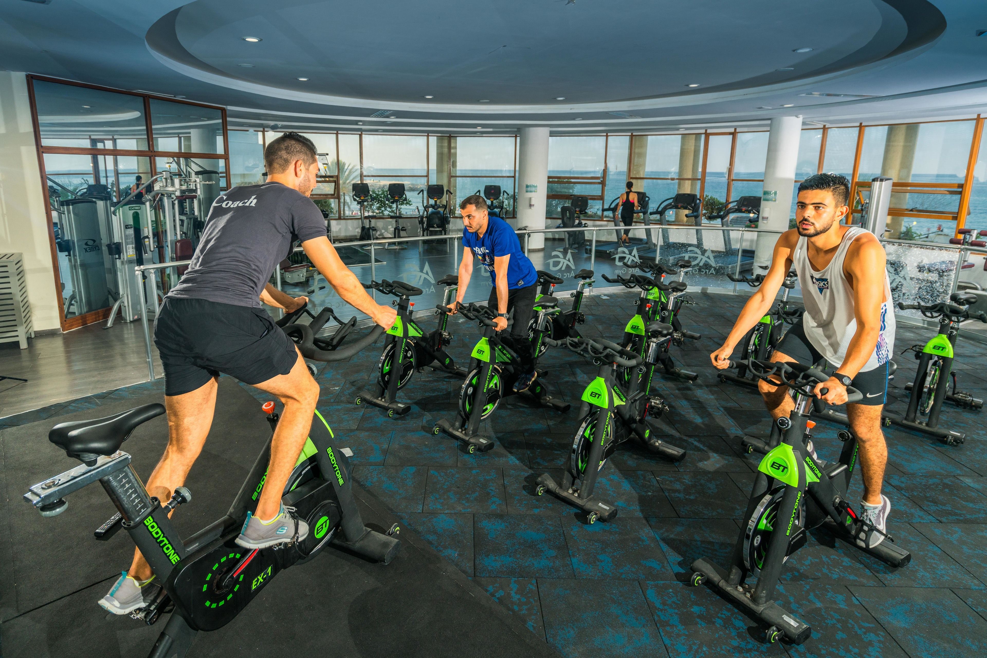A gym with stationary bikes, weight machines, and a large window overlooking the ocean.