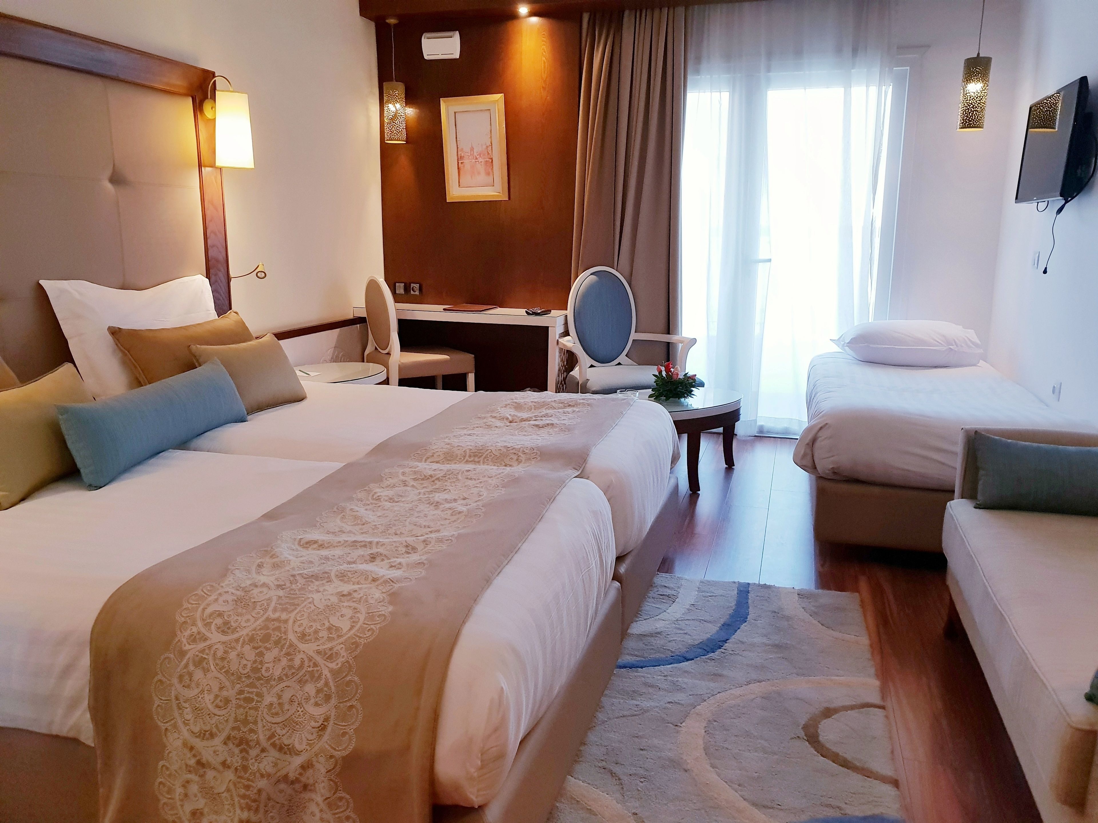 A hotel room with two beds, a desk, a chair, and a TV.