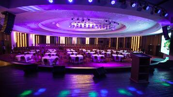 A large, circular auditorium with rows of tables and chairs, equipped with stage lighting and a podium.