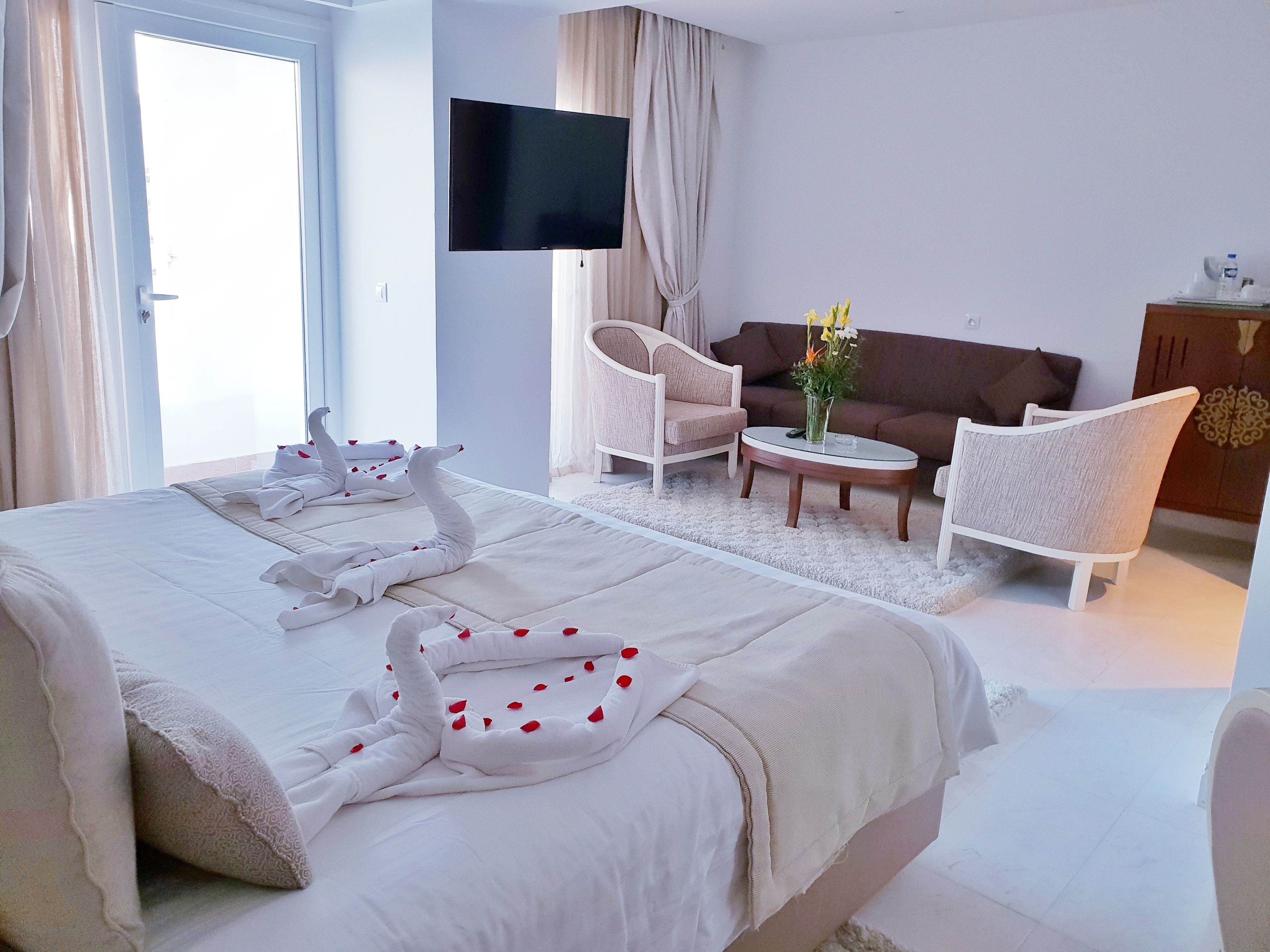 Une chambre d’hôtel avec un grand lit, un téléviseur à écran plat, un canapé, deux fauteuils et une petite table ronde.