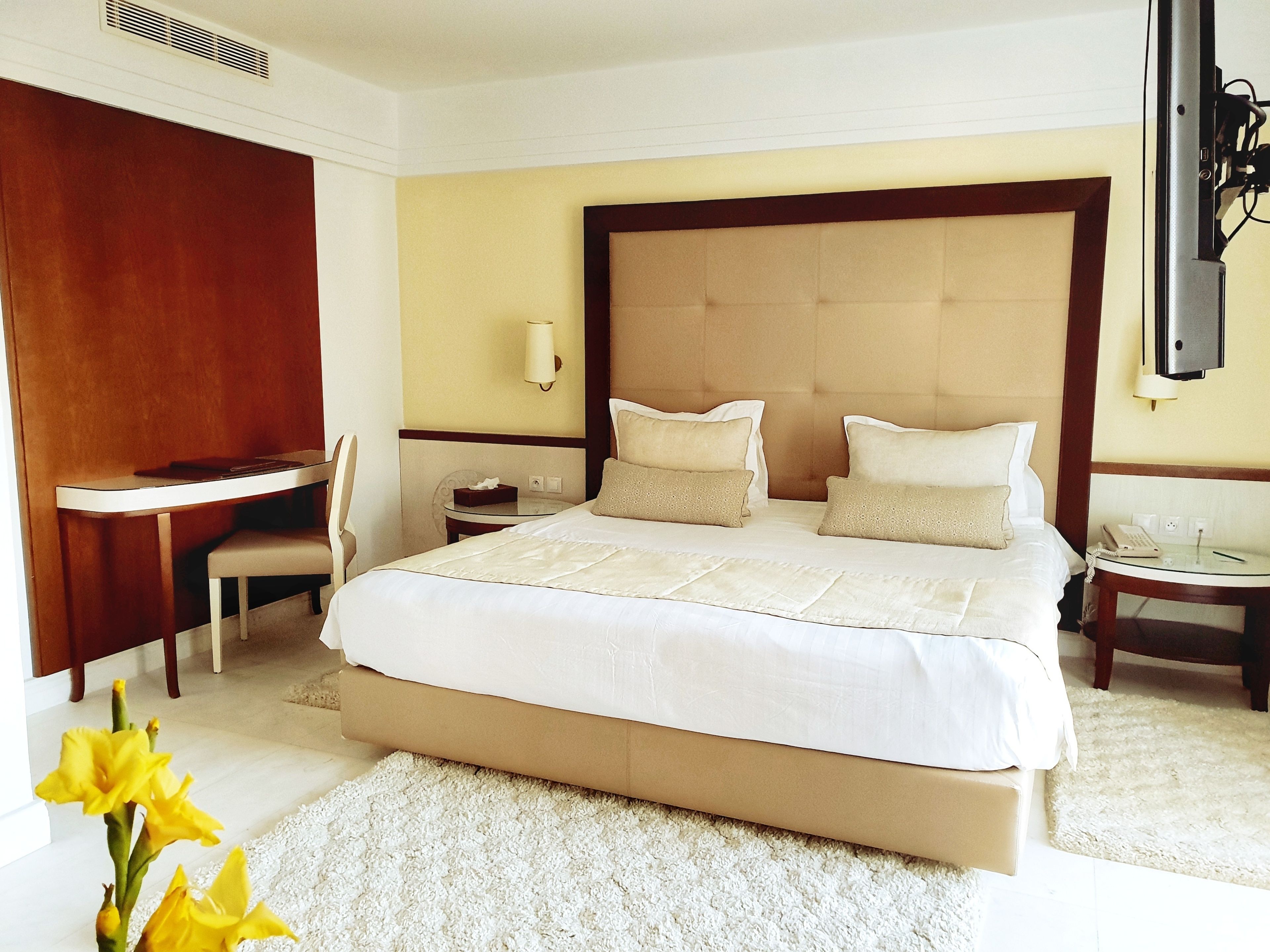 Habitación de hotel con una cama grande, un escritorio, una silla, una mesita de noche y un televisor instalado en la pared.