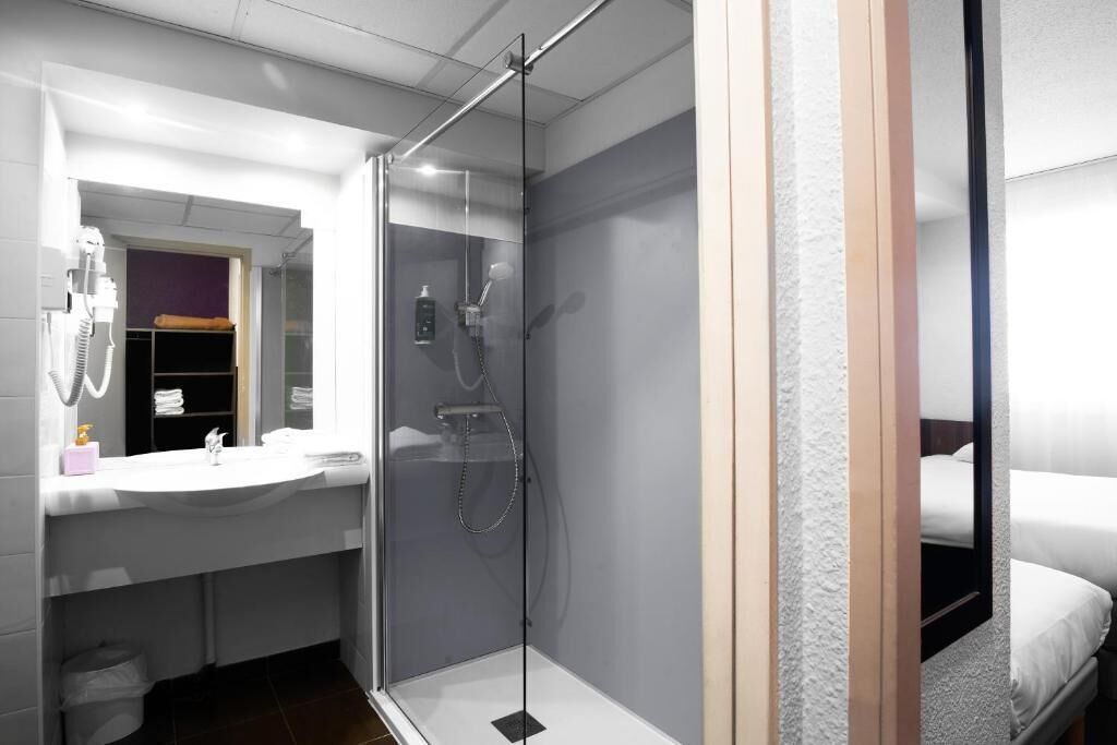 Een moderne badkamer met een douche met glazen wand, een witte wastafel en een spiegel erboven.