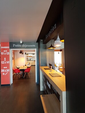 A hotel reception area with a wooden reception desk, a sign for 'Petits déjeuners' (breakfast), and directional signs for rooms 101-120, 122-141, and 200-241. - Brit Hotel Confort Montpellier Parc Expositions (Perols)