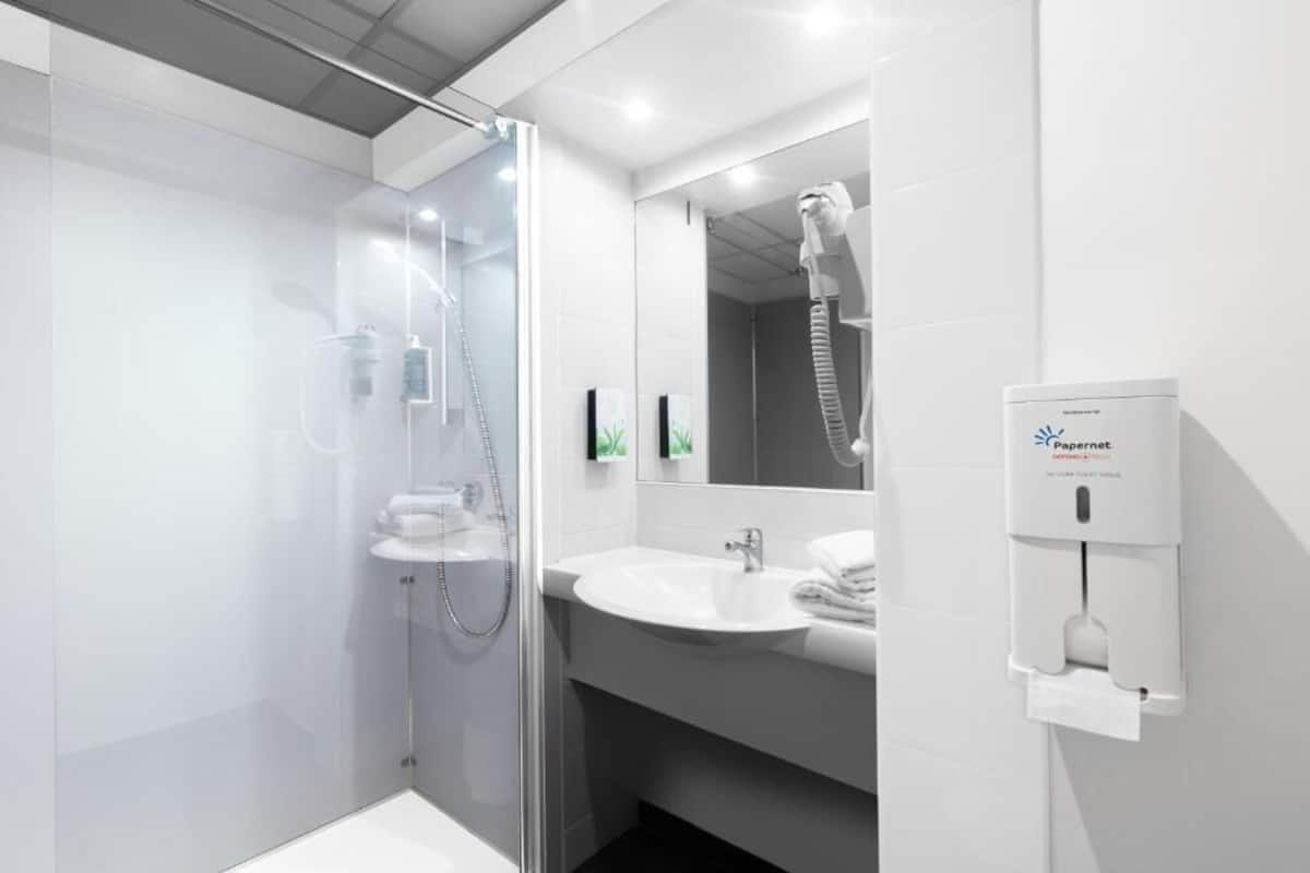 Uma casa de banho moderna com cabine de duche em vidro, lavatório branco e dispensador de papel.