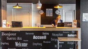 A hotel reception desk with a sign reading "Réception" and multiple welcome signs in various languages. - Brit Hotel Confort Montpellier Parc Expositions (Perols)