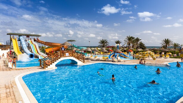 A large outdoor swimming pool with multiple slides and water features, surrounded by lounge chairs and umbrellas. - Tui Magic Life Penelope Beach (Djerba Midun)