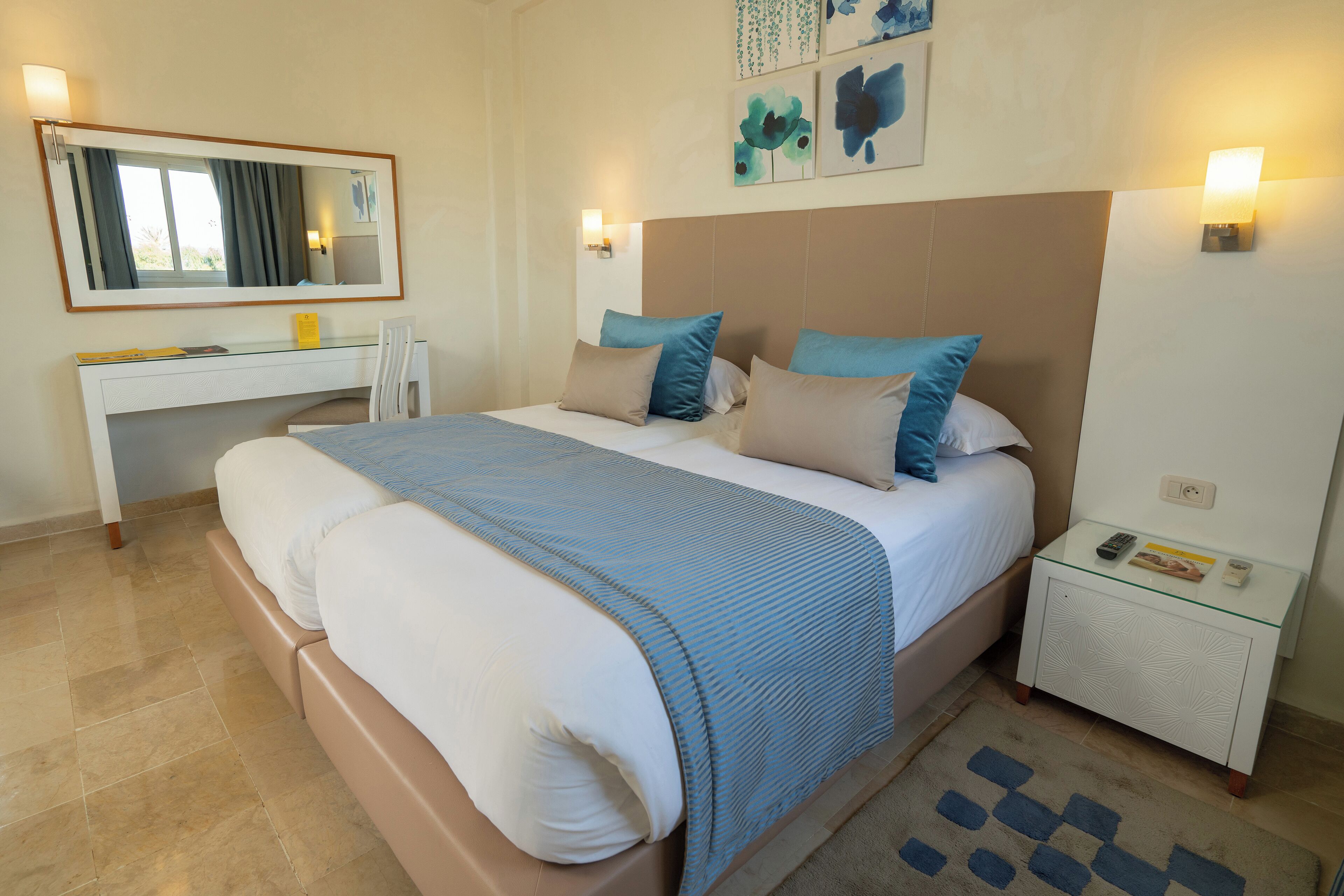 A bedroom with a large bed, a bedside table, a nightstand, a desk, and a mirror.