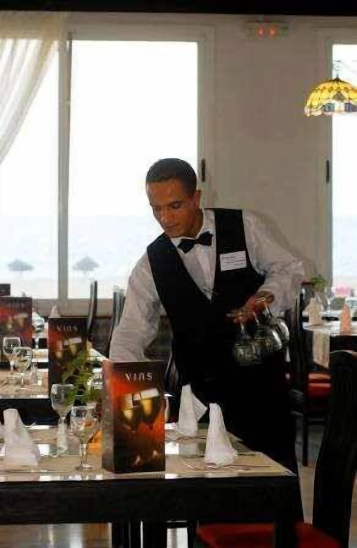 A waiter serving a drink at a table with a view of the ocean.