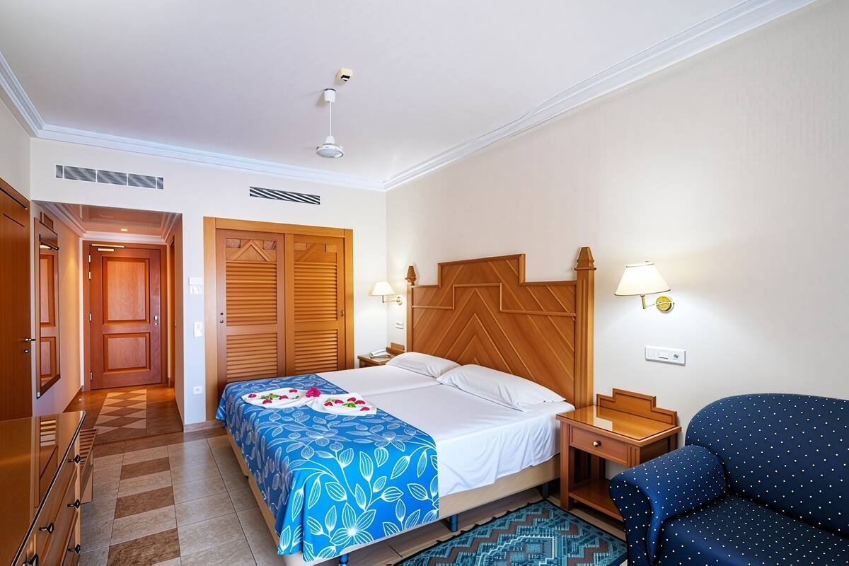 A hotel room with a bed, two nightstands, a desk, a chair, and a wardrobe.