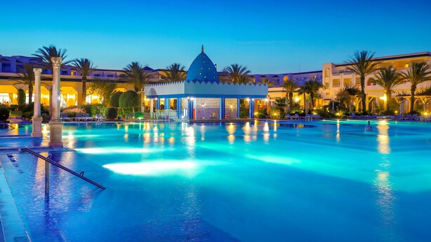 A swimming pool with a gazebo in the center, surrounded by palm trees and hotel buildings. - Hotel Marco Polo (Hammamet)