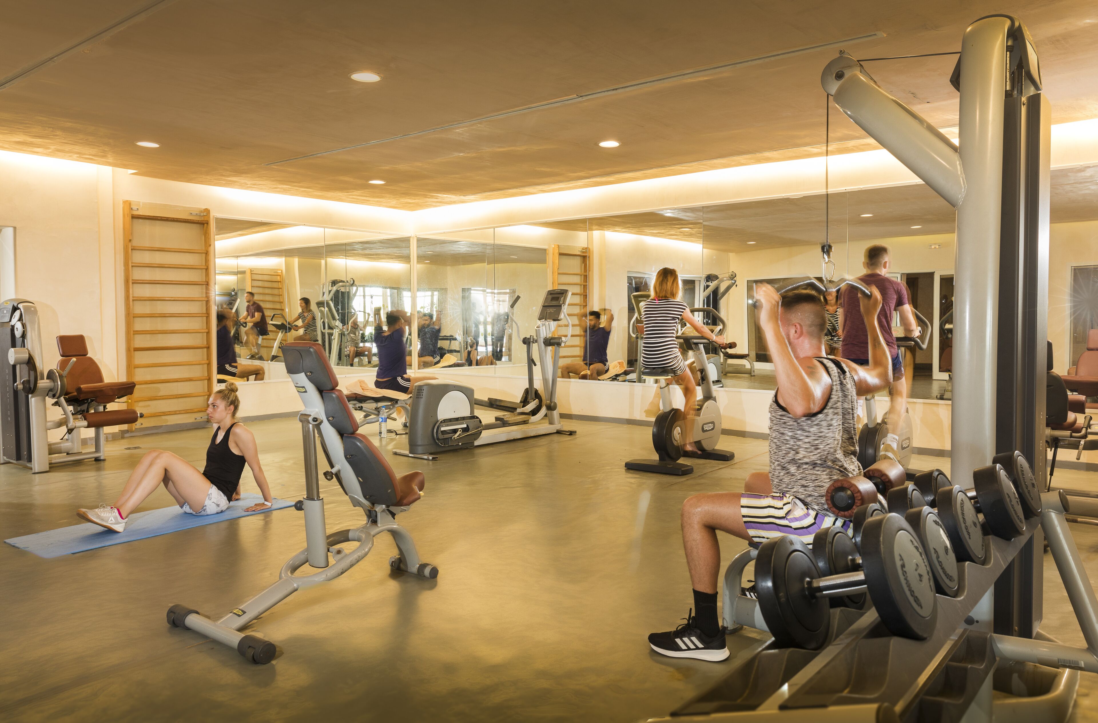 A gym with various exercise equipment, a mirrored wall, and a wooden floor.