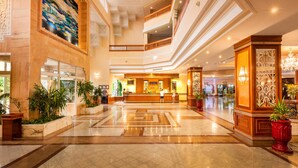 A spacious lobby with a high ceiling, a reception desk, and a staircase leading to an upper floor. - Hotel Marco Polo (Hammamet)