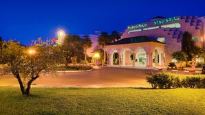 A building with a sign reading "MARCO POLO" and Arabic text, surrounded by well-maintained lawns and palm trees. - Hotel Marco Polo (Hammamet)