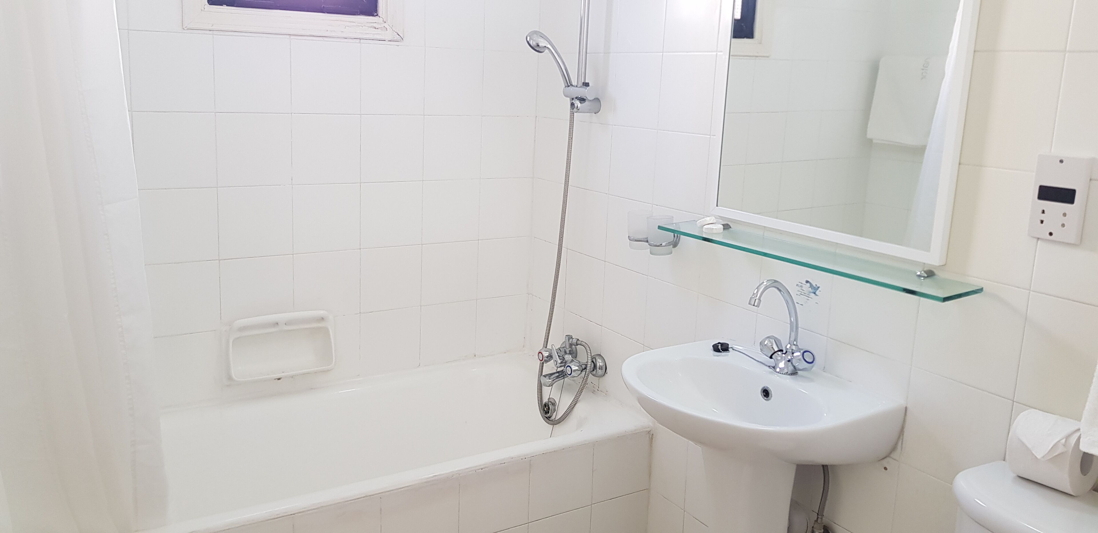 Un baño moderno con bañera, un estante de vidrio sobre el lavabo y un espejo.