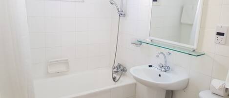 Un baño moderno con bañera, un estante de vidrio sobre el lavabo y un espejo.