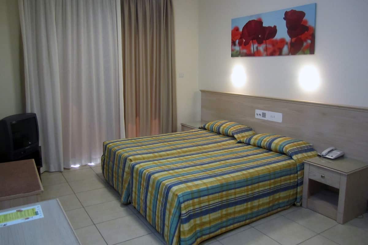 Una camera d'albergo con un letto, un comodino, una scrivania, una sedia e un quadro appeso al muro.