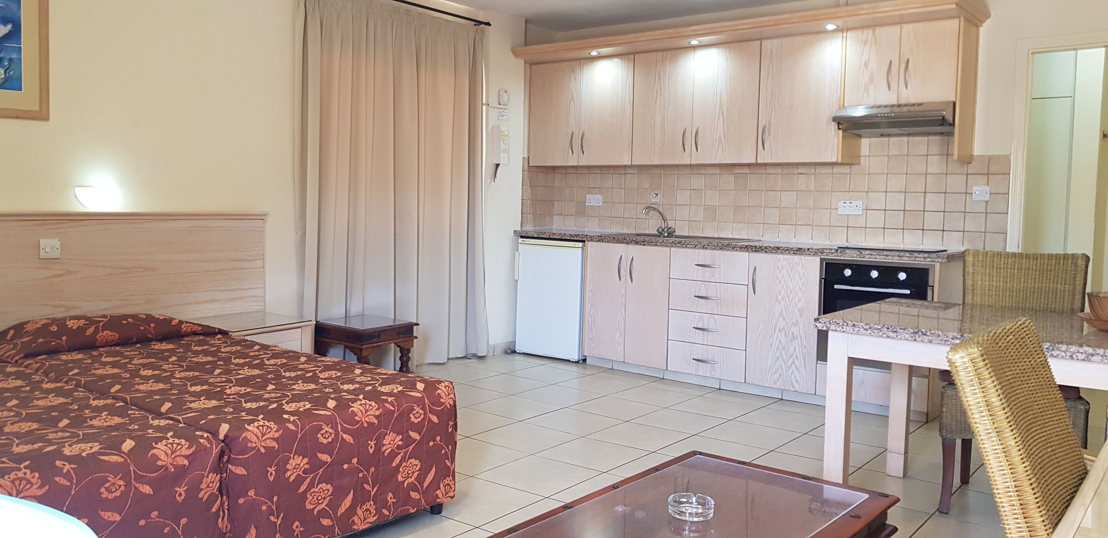 Een hotelkamer met een bed, een kleine tafel, een eettafel met stoelen, een kitchenette en een badkamer.